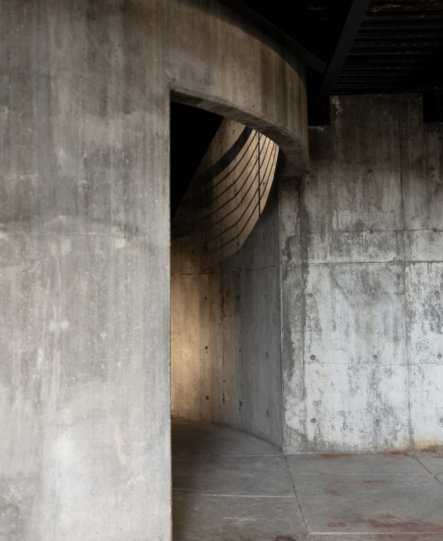 Curved concrete hallway with shadows cast by a railing on the inner wall.