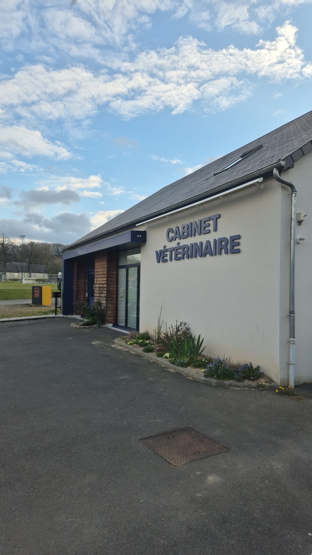 Exterior of a veterinary clinic building with a sign reading 'CABINET VÉTÉRINAIRE' under a partly cloudy sky.