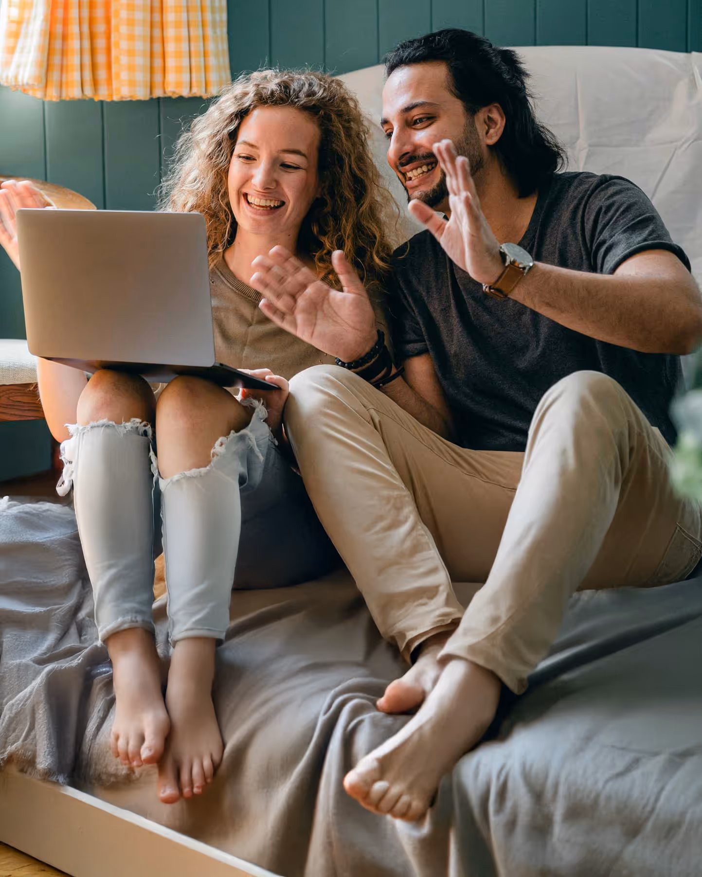 Couple sitting on a bed video calling someone on a laptop