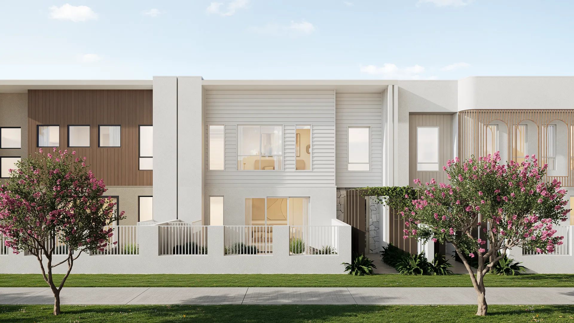 Row of modern two-story townhouses with garages, large windows, trees, and green lawn in front under a blue sky.