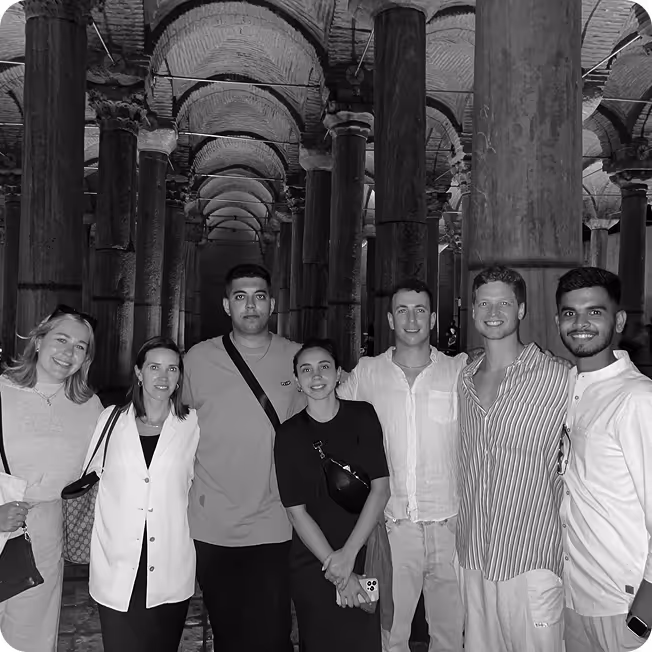 Group of seven young adults standing and smiling inside an ancient vaulted structure with tall columns.