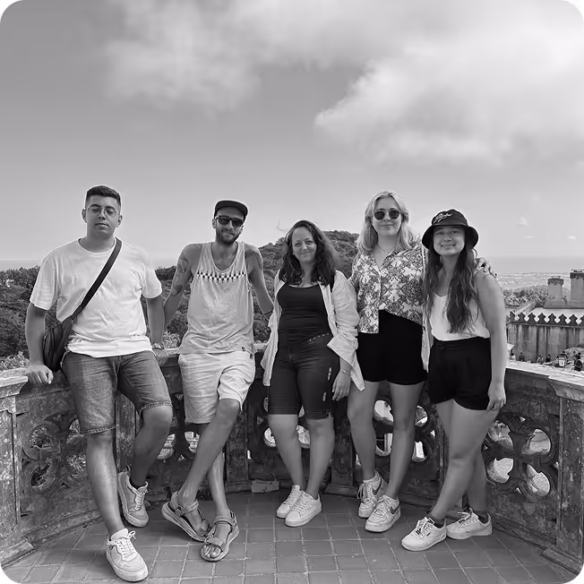 Five young adults standing in a row outdoors by a decorative stone railing with a scenic landscape in the background.