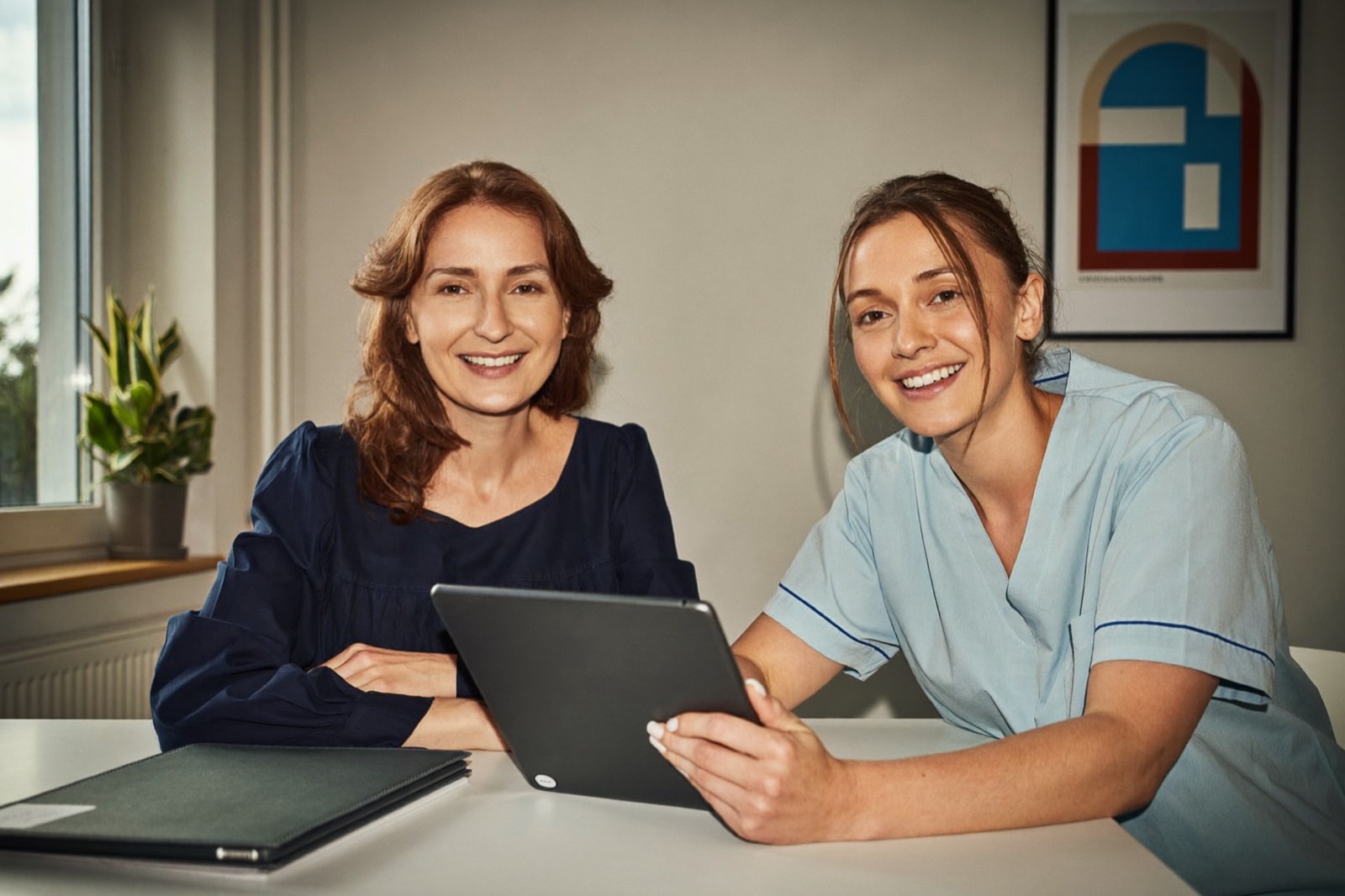 Praxismanagerin und Zahnmedizinische Fachangestellte in hellblauer Kleidung sitzen im Praxisbüro nebeneinander und besprechen am Tablet Cloud-Zahnarztsoftware und Datenhaltung