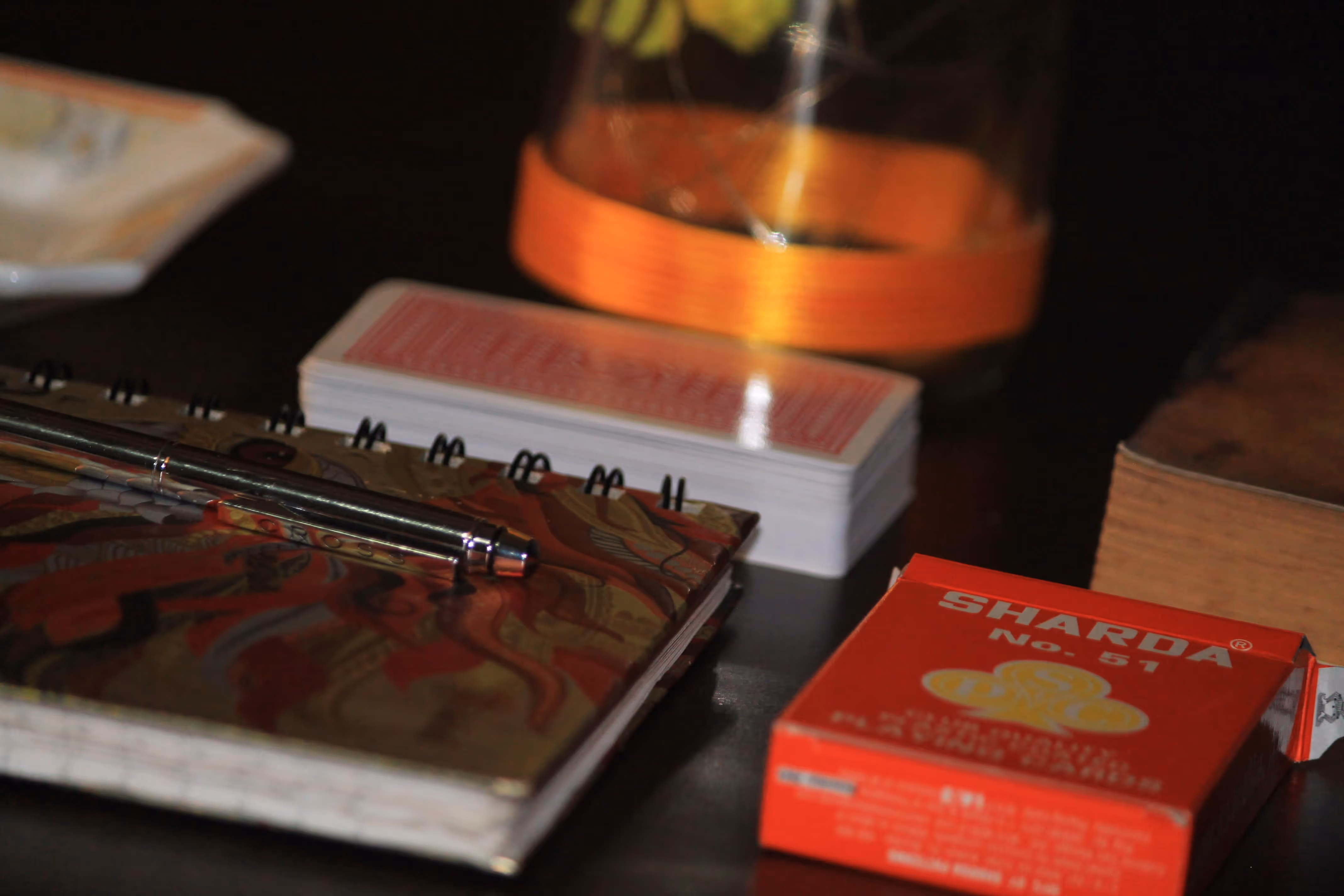 Sharda No. 51 deck placed beside an open book and a glass bottle under warm evening light, evoking calm and timeless simplicity.