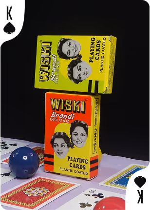Two Wiski Brandi tuck boxes stacked on top of each other, surrounded by scattered playing cards, creating a bold and nostalgic display