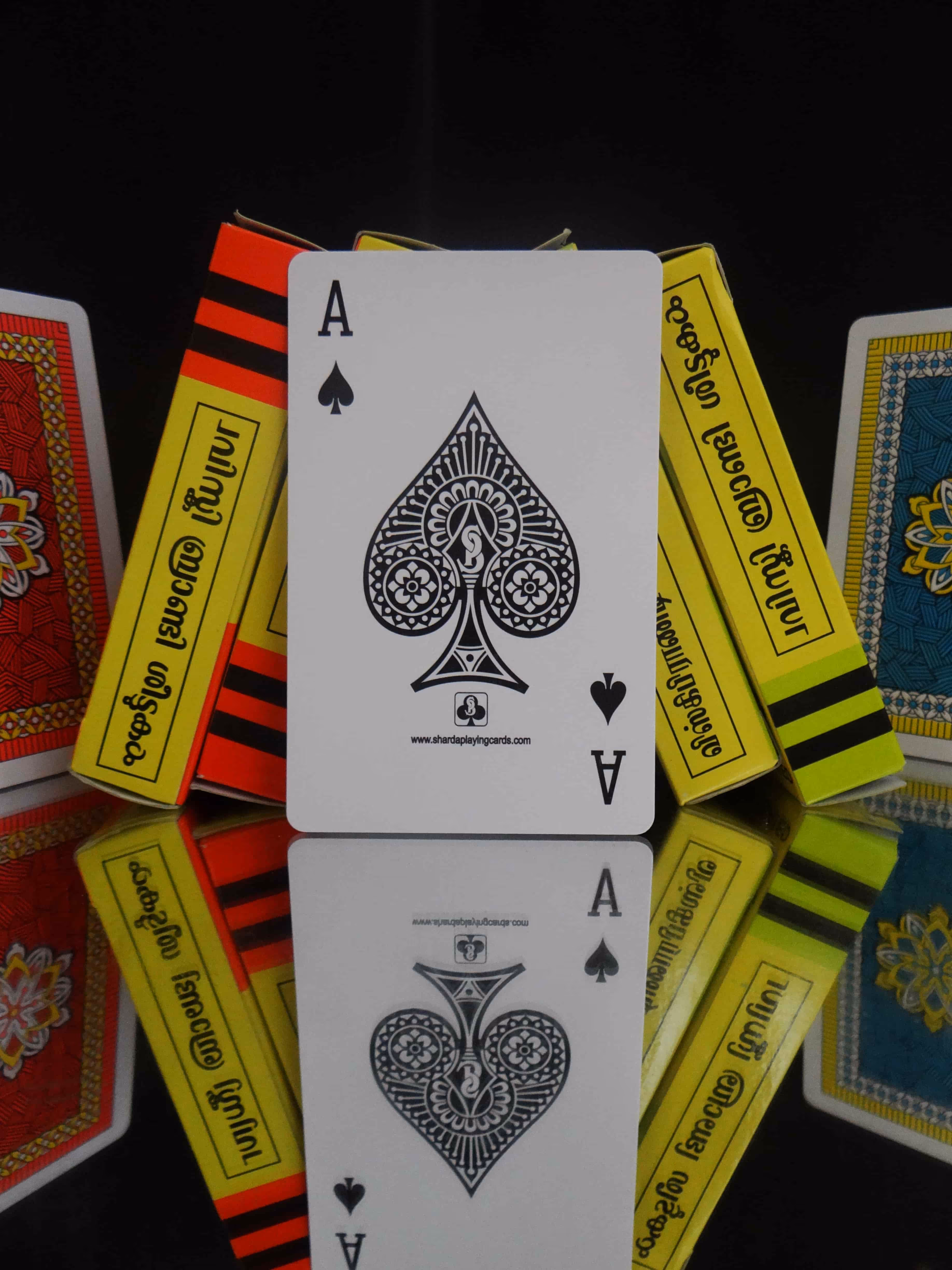 Red and yellow Wiski Brandi tuck boxes placed side by side with the Ace of Spades in the center, positioned on a mirror surface reflecting the deck’s elegant design and intricate detailing.