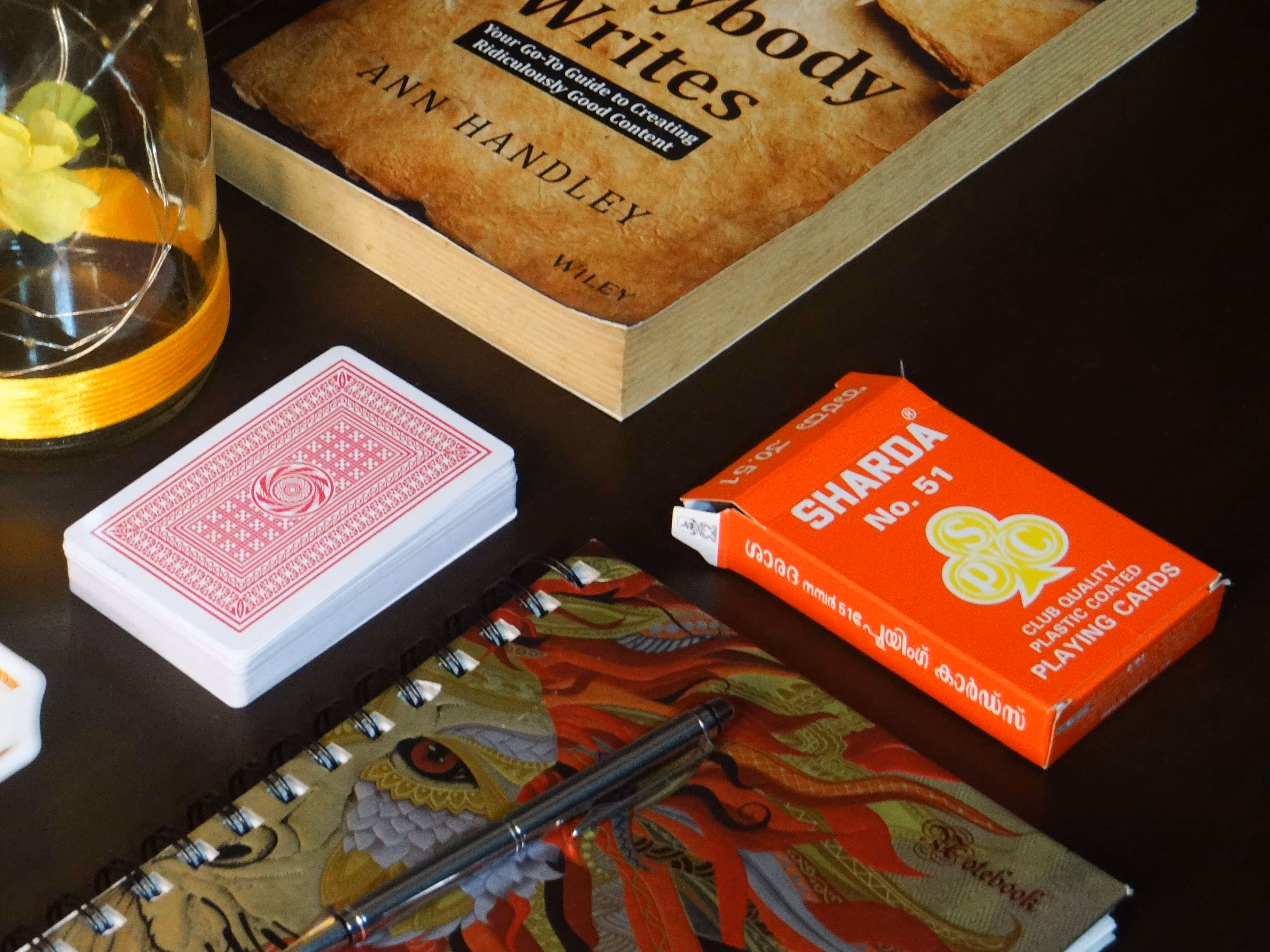 Sharda No. 51 deck placed beside an open book and a glass bottle under in soft light.