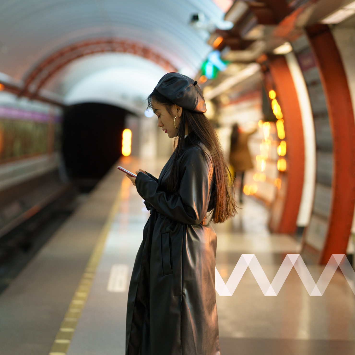 Woman stands on metro platform using her phone.