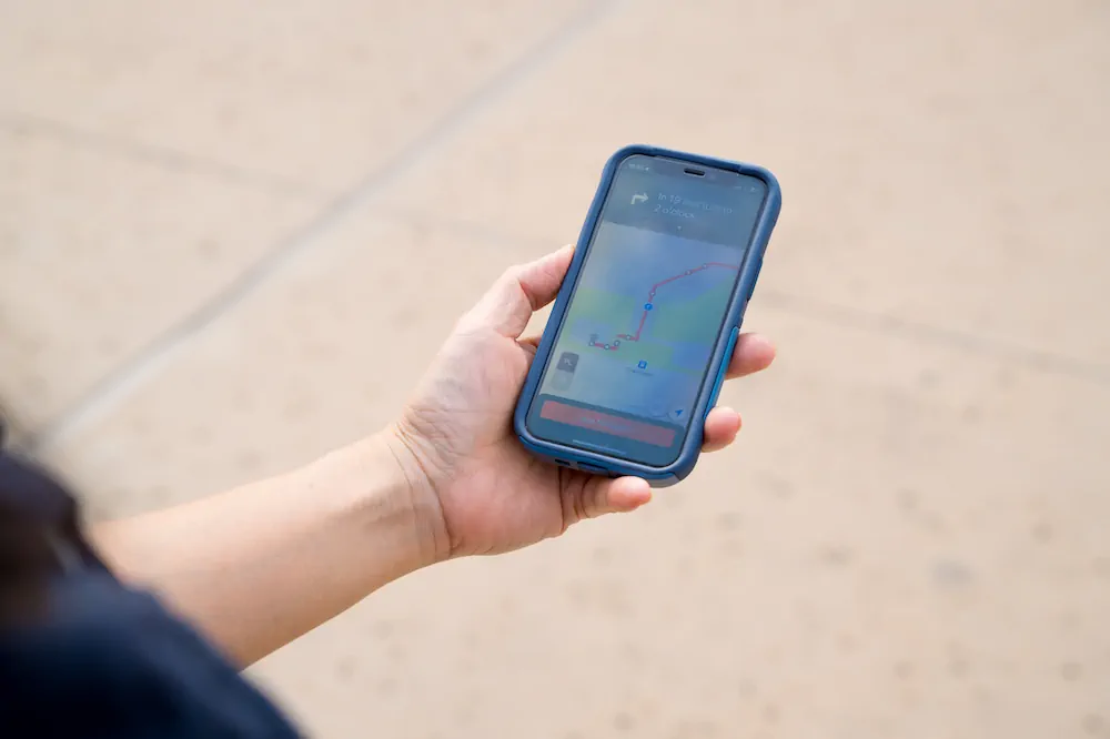 A photo of a woman's hand with a smartphone screen showing the Waymap app navigating a route.