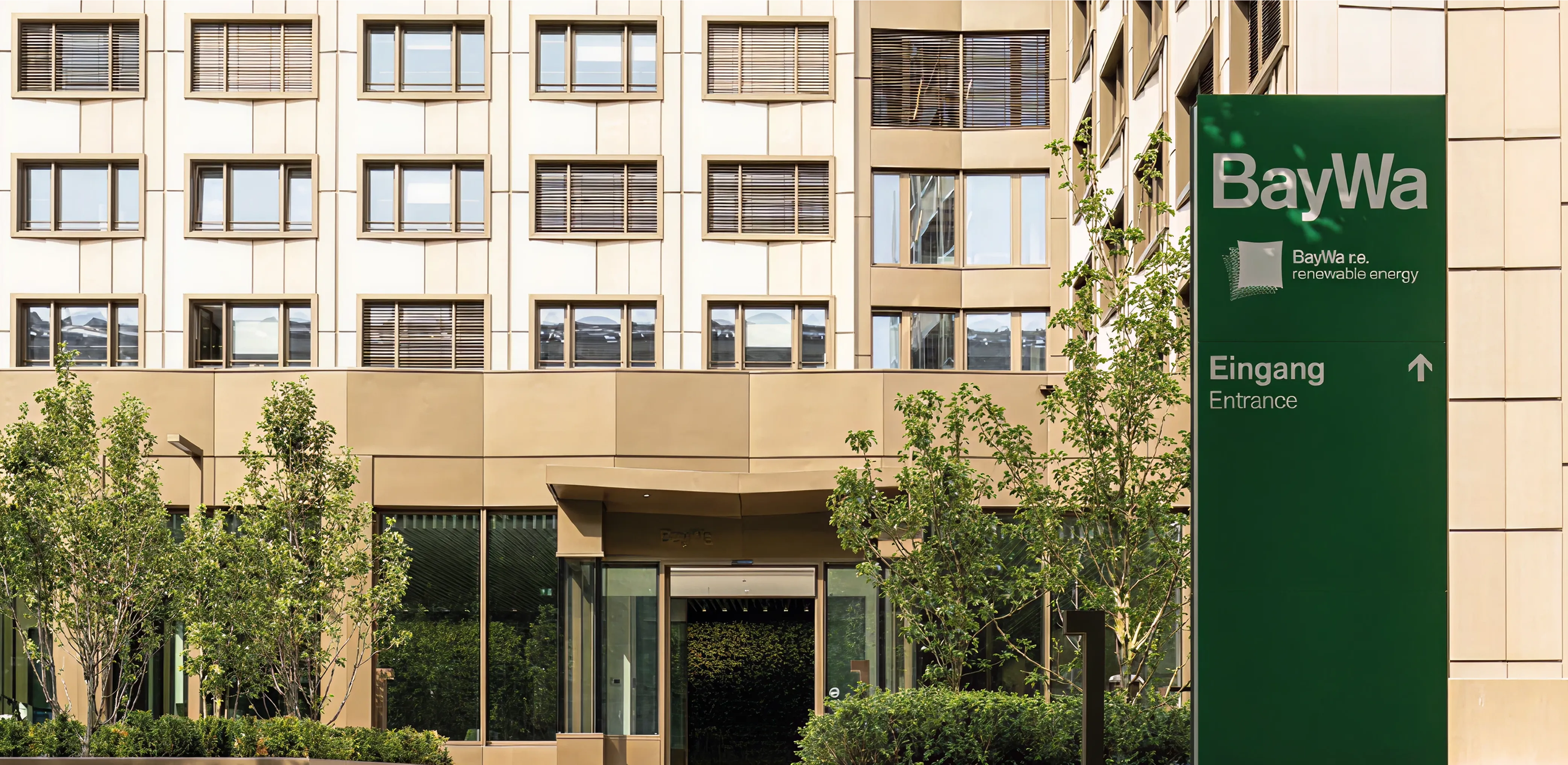 Modern beige office building with multiple windows and green BayWa entrance sign with trees in front.