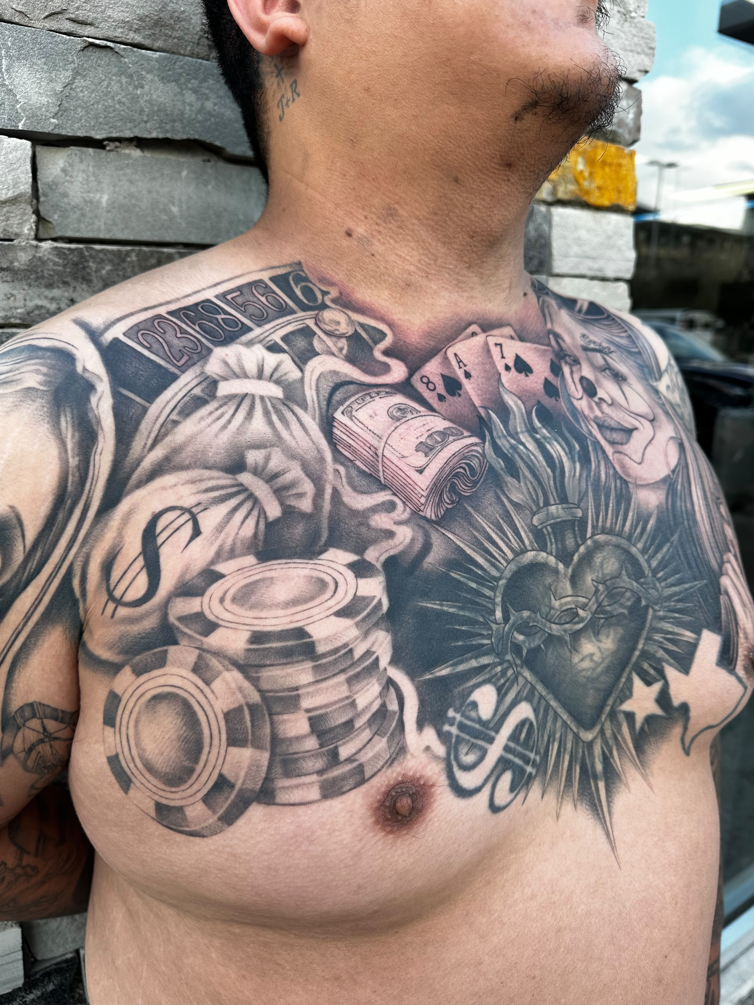 Casino chips and money bags chest tattoo in black and grey by Dani B at Santana Studio Co