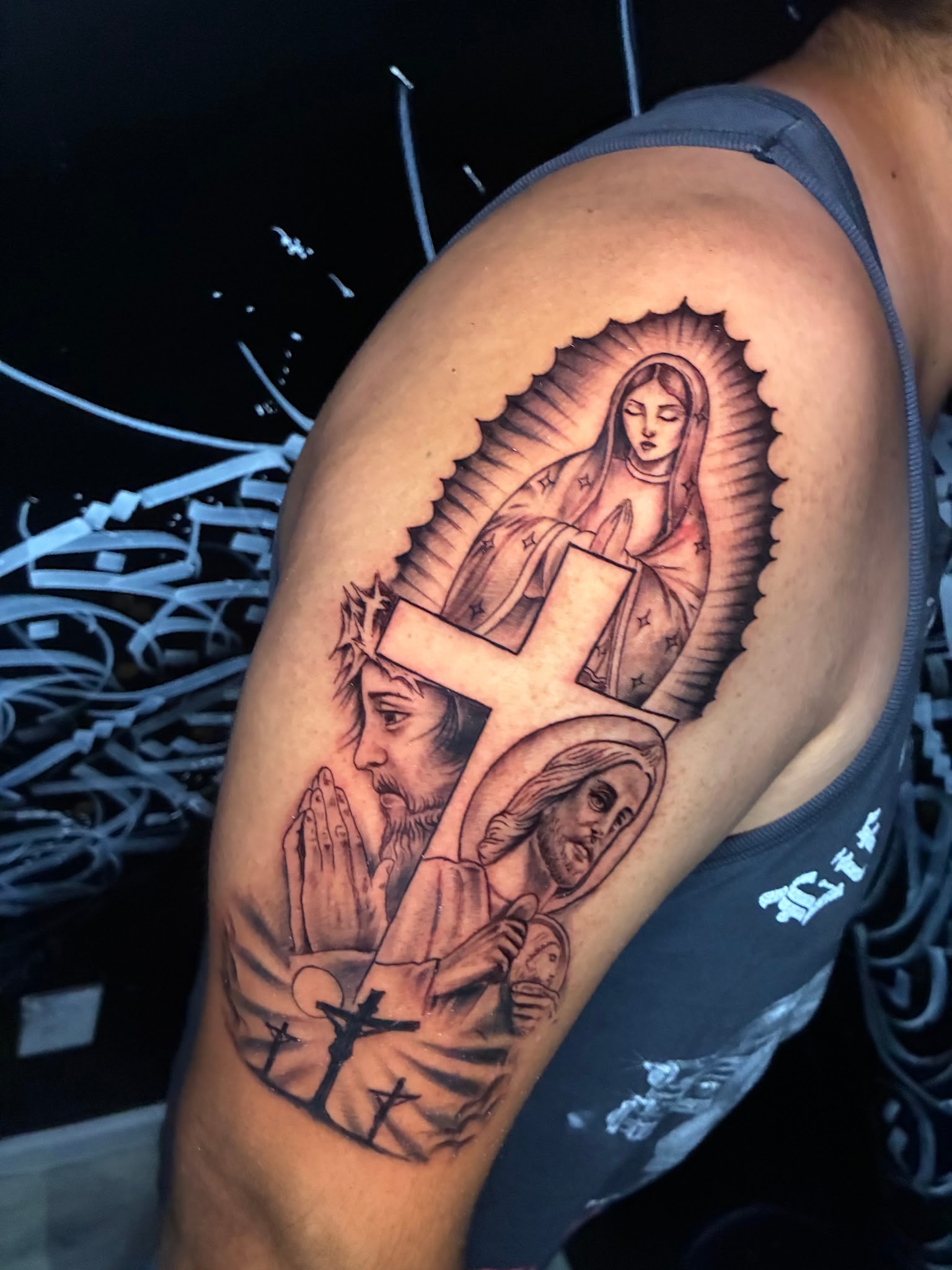 Black and grey Virgin of Guadalupe and Jesus religious upper arm tattoo by Jessica at Santana Studio Co, Fort Worth