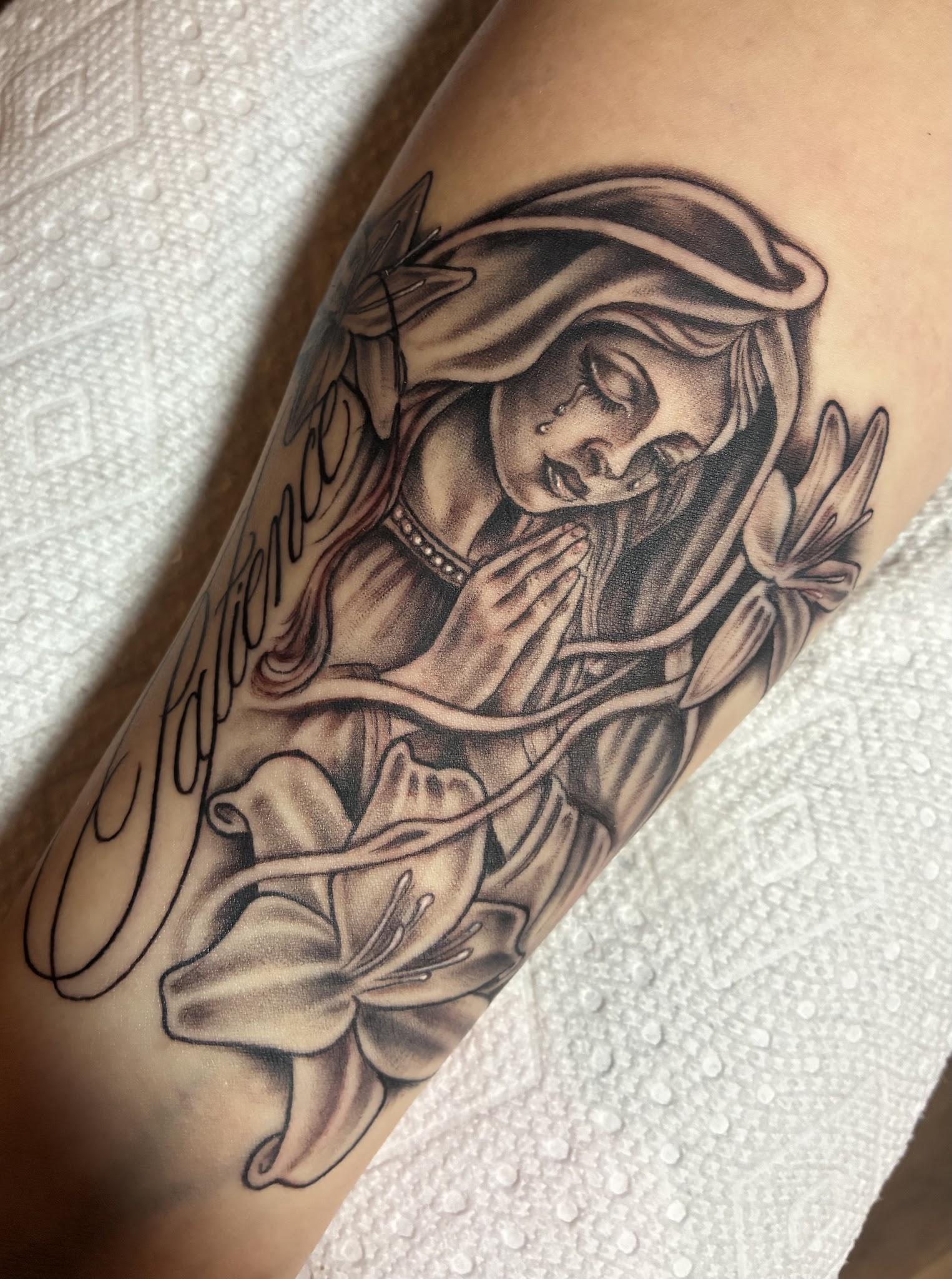 Virgin Mary with lilies and Patience script forearm tattoo in black and grey by Jessica at Santana Studio Co