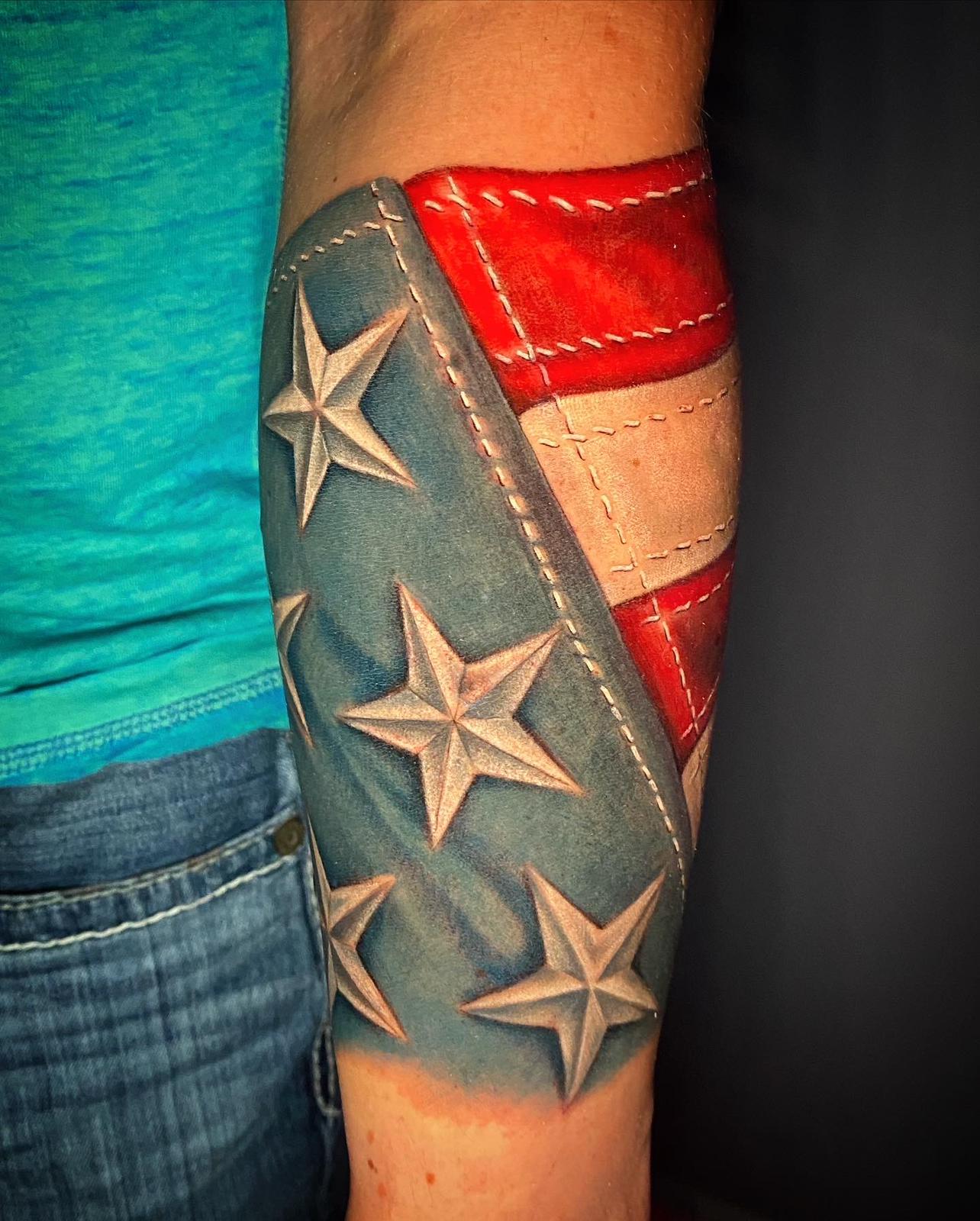 Color American flag forearm tattoo with leather and stitching detail by RESN, Fort Worth tattoo artist