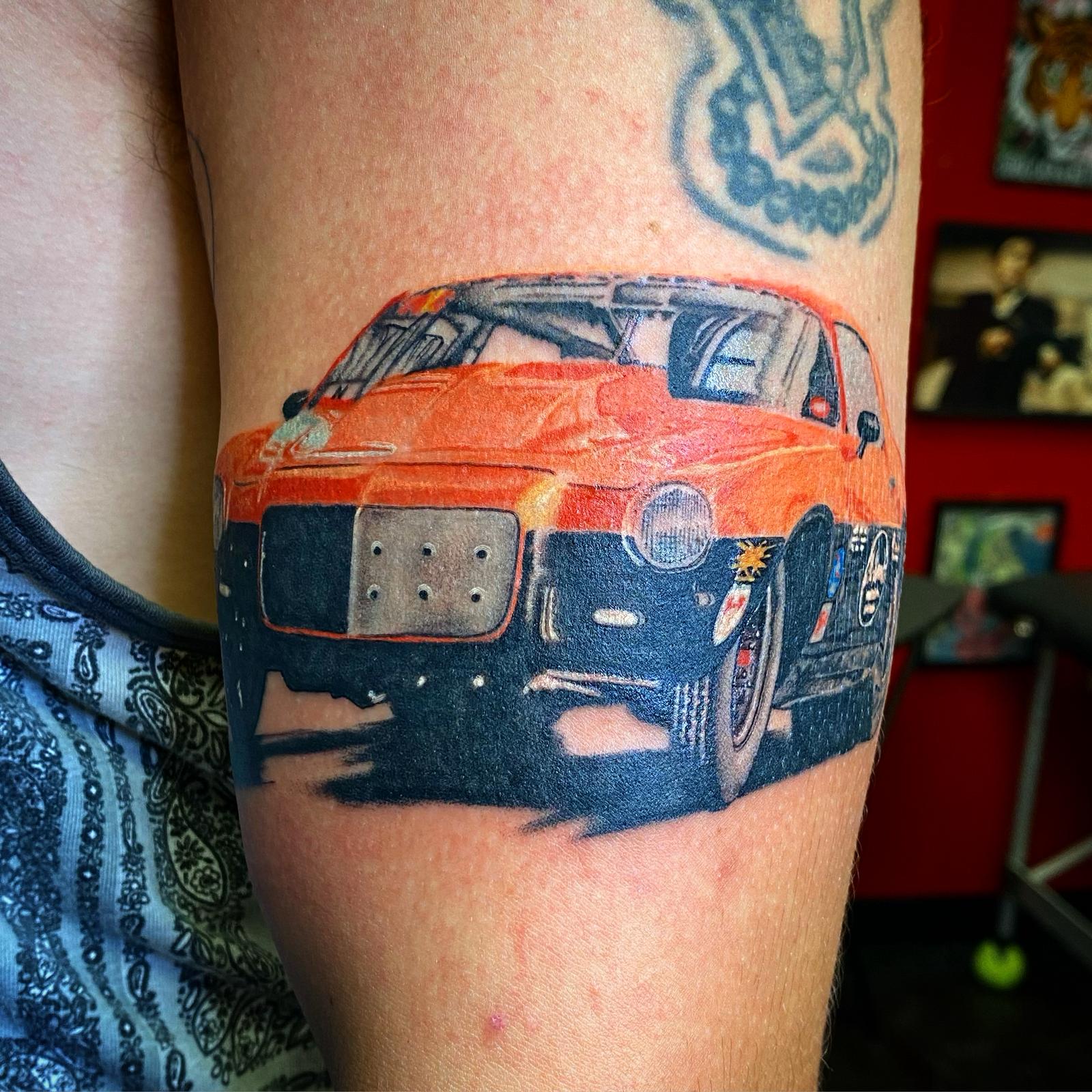 Color realism tattoo of an orange and black race car on the upper arm by RESN at Santana Studio Co, Fort Worth