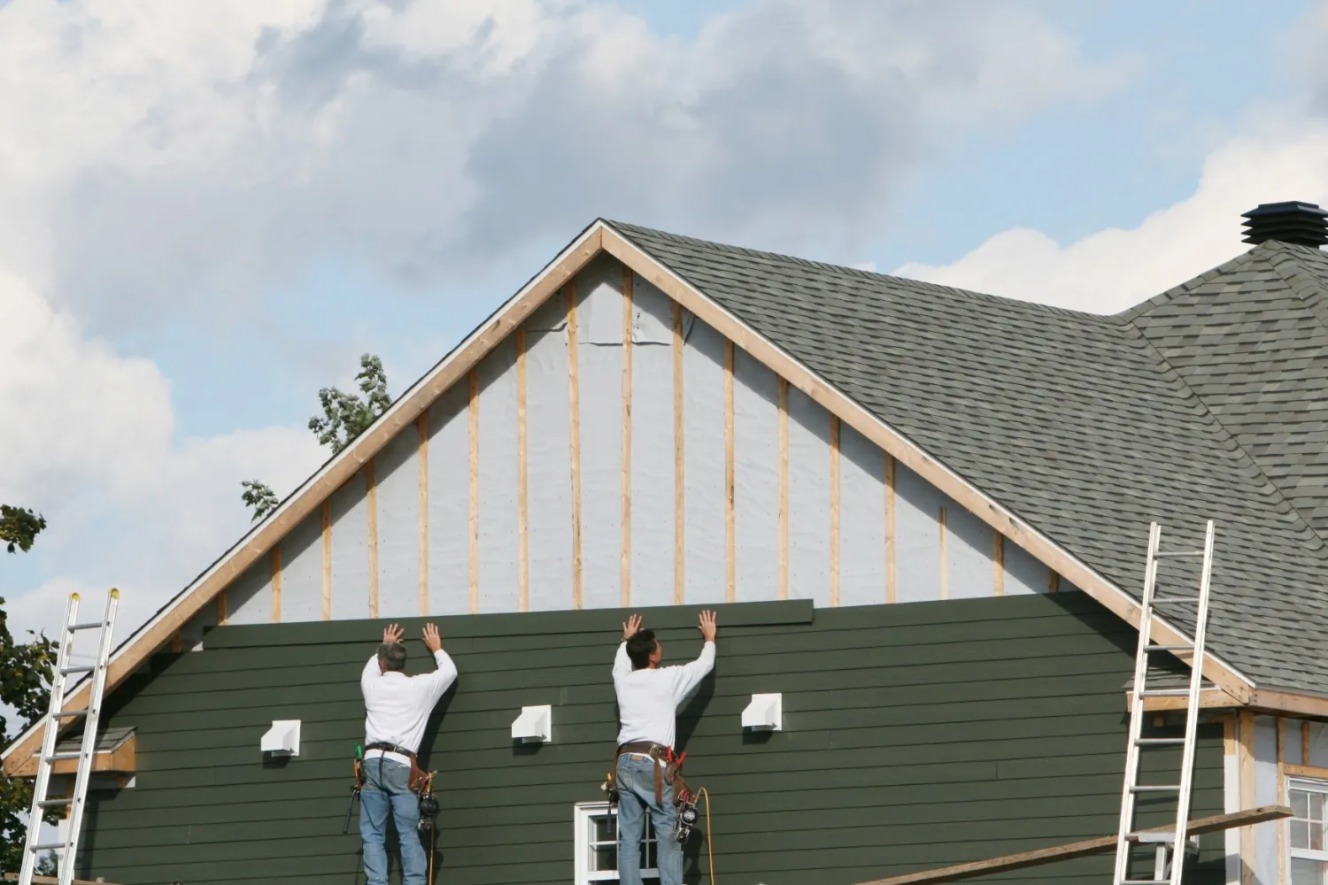 Two men working together on the roof of a house, wearing safety gear and focused on their task.