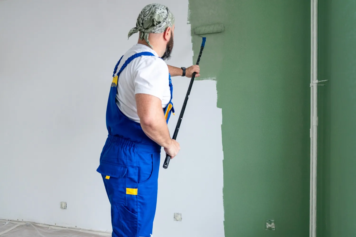 A man in overalls painting a room with green paint.