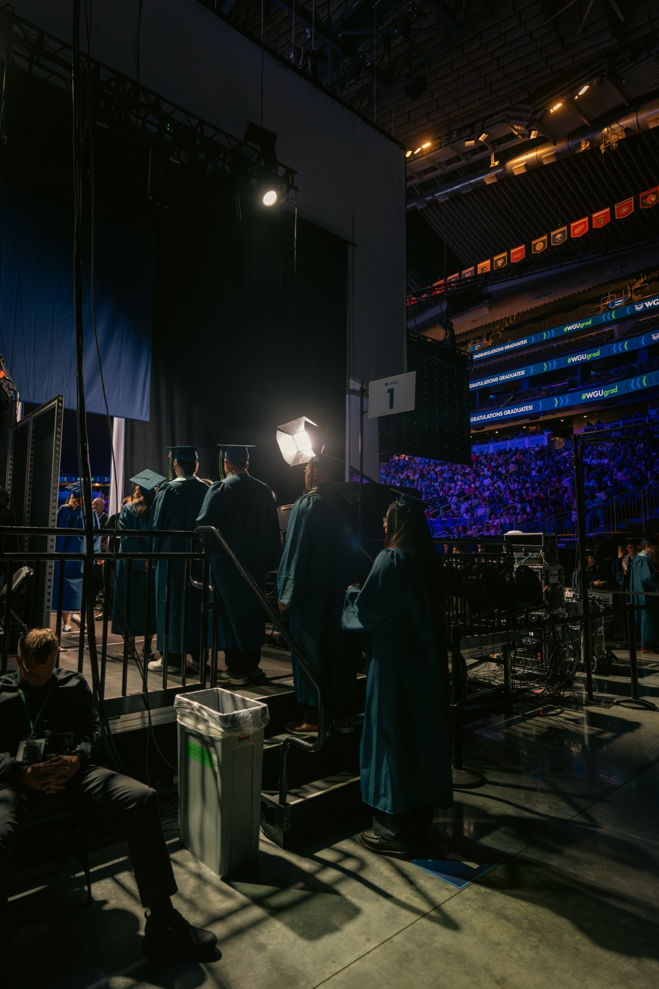 Arena commencement stage with graduates and camera crew at the podium