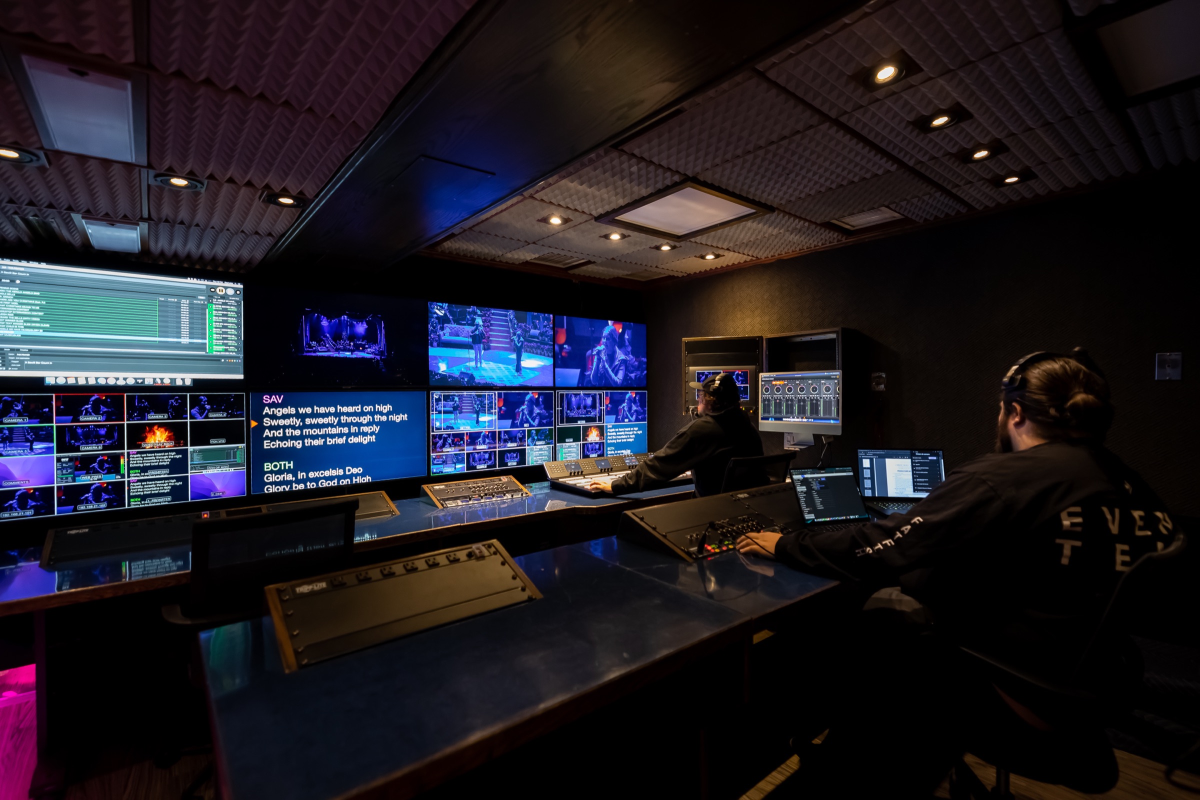 Two operators at the video switcher and monitor wall inside the large broadcast truck
