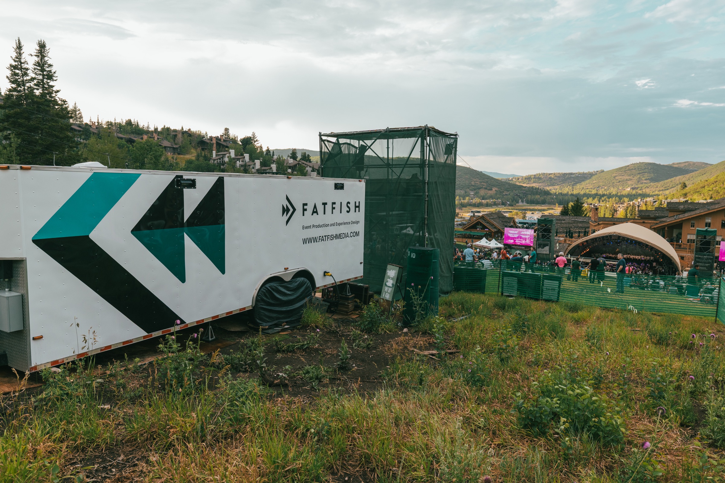 Small broadcast trailer parked on a hillside beside an outdoor amphitheater stage
