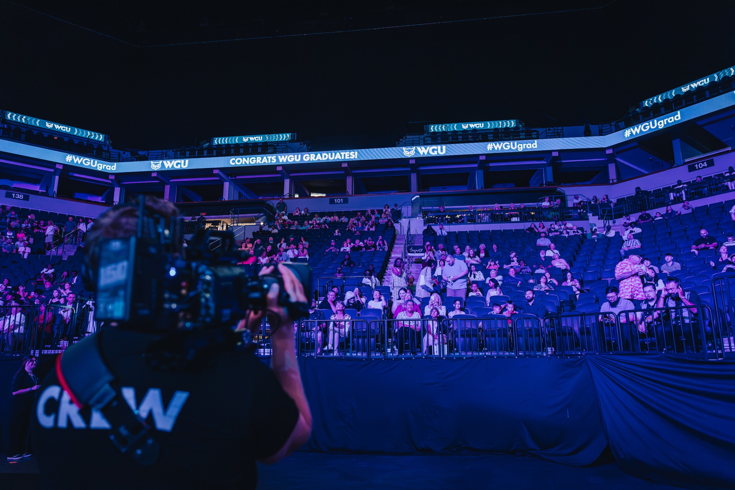 Camera operator shooting the crowd from the arena floor at a WGU commencement