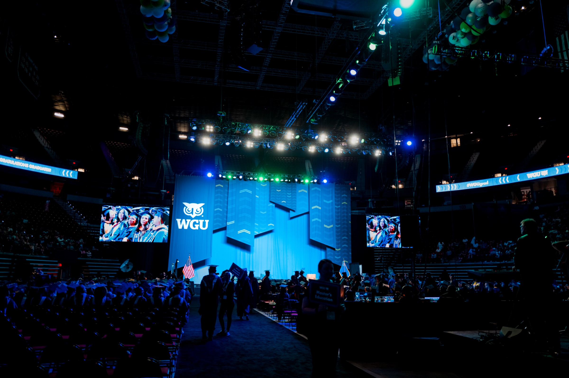 WGU commencement stage washed in blue light with the owl logo and chevron scenic panels as graduates process in