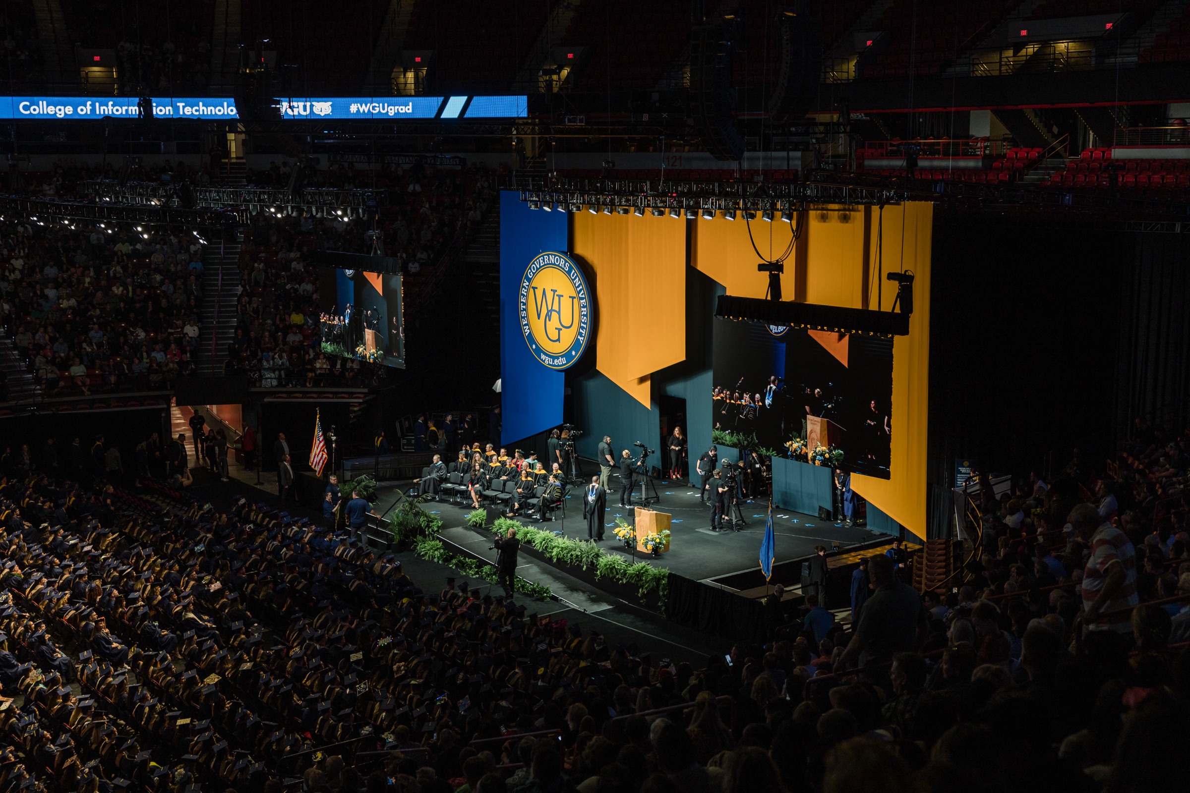 WGU commencement stage in a packed arena with gold and navy scenic panels and the university seal