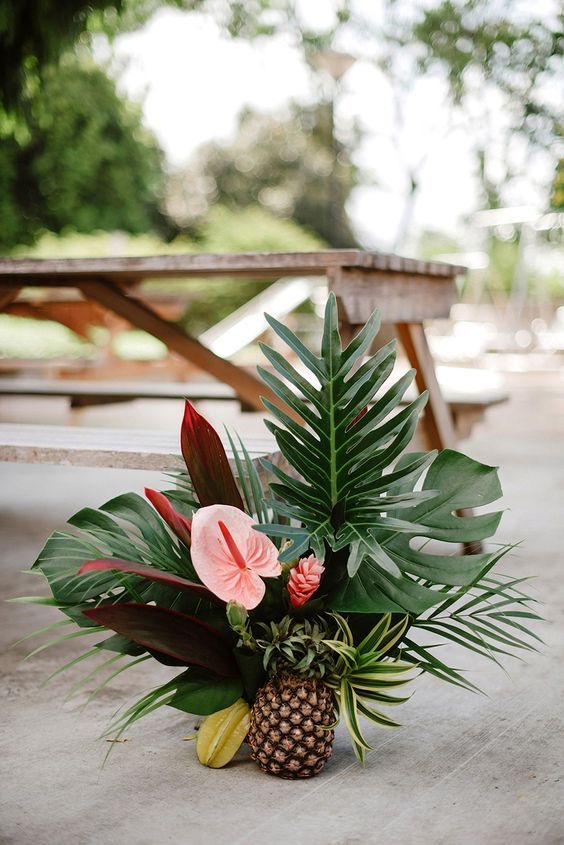 Tropical arrangement of monstera, palm and anthurium in a pineapple base