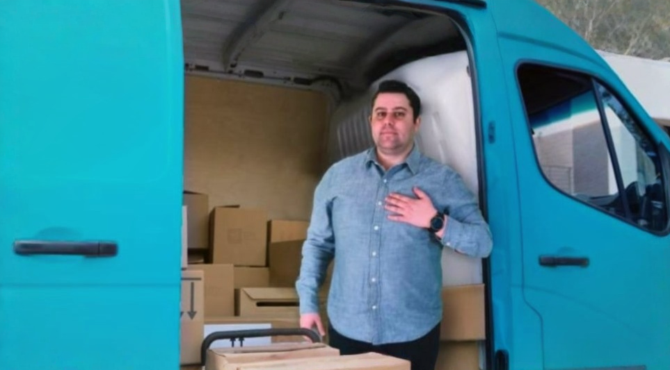 Man in a blue shirt standing inside a turquoise delivery van with cardboard boxes around him.