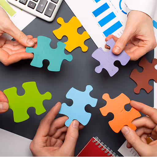 Manos sosteniendo piezas de rompecabezas de colores variados sobre una mesa con documentos y calculadora.