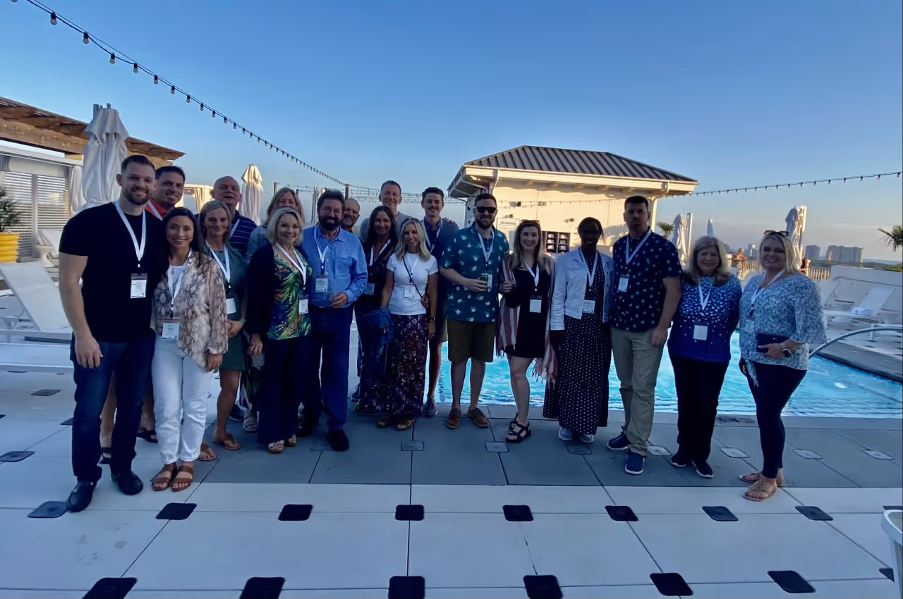 Group of people standing together by a rooftop pool under clear blue sky.