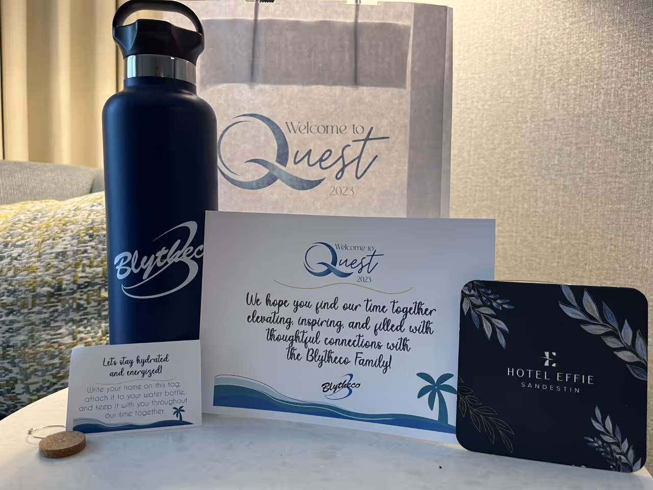 Welcome bag with a dark water bottle, event cards, and a Hotel Effie Sandestin key card on a round table.
