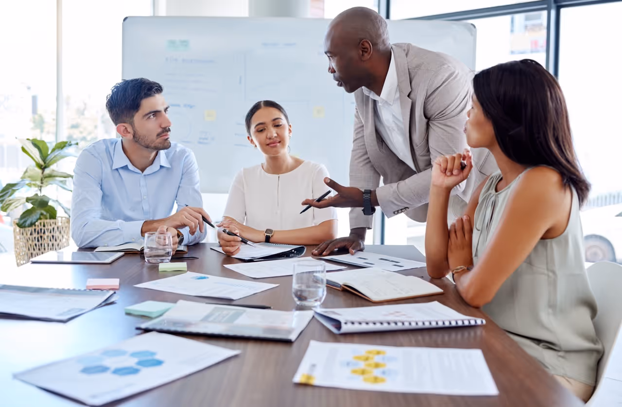 A diverse group of four professionals having a meeting around a table with documents and notebooks.