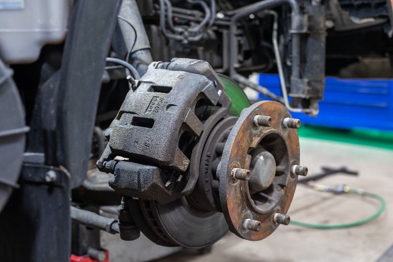 Close-up of a heavy-duty truck wheel hub and brake assembly during repair, showing rotor, caliper, and exposed wheel studs.