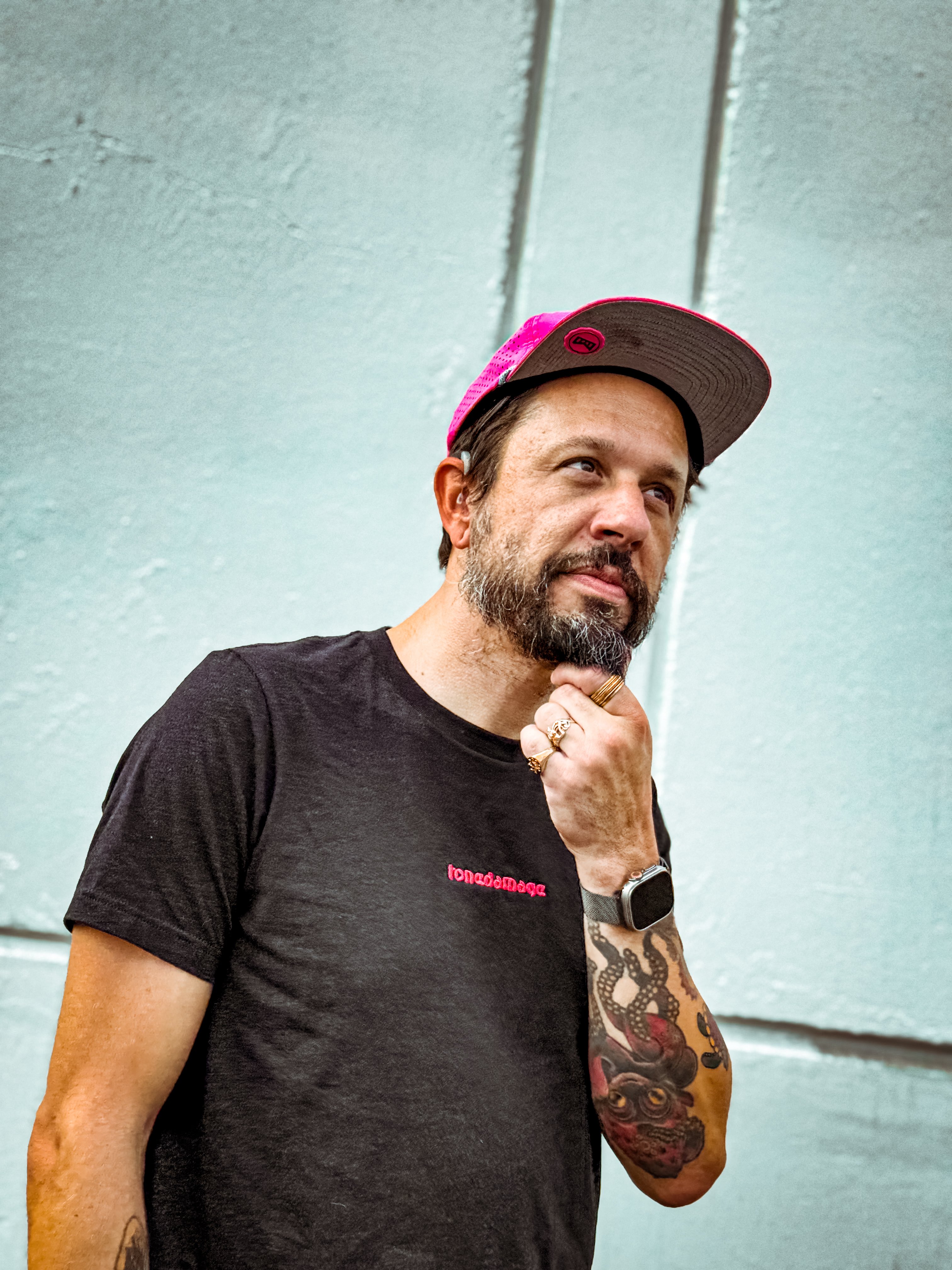 A middle-aged man strokes his beard with his left hand while smiling to the right of the camera.