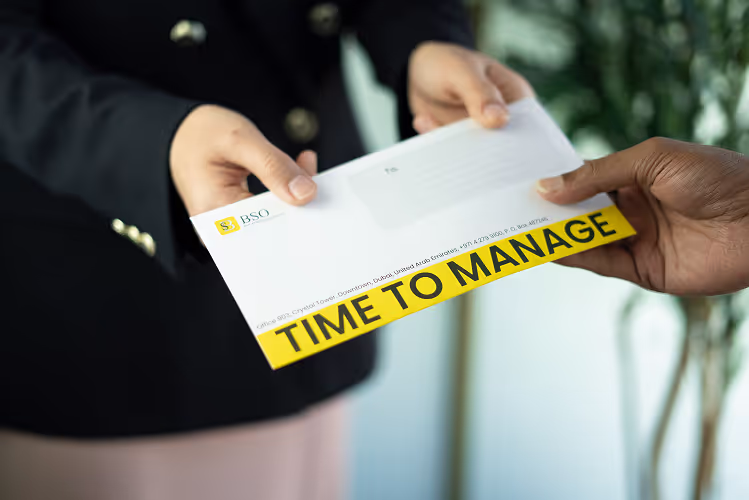 A close-up of hands exchanging a white envelope with the BSO logo and 'TIME TO MANAGE' printed on it, symbolizing the start of a service provided by property management in Dubai.