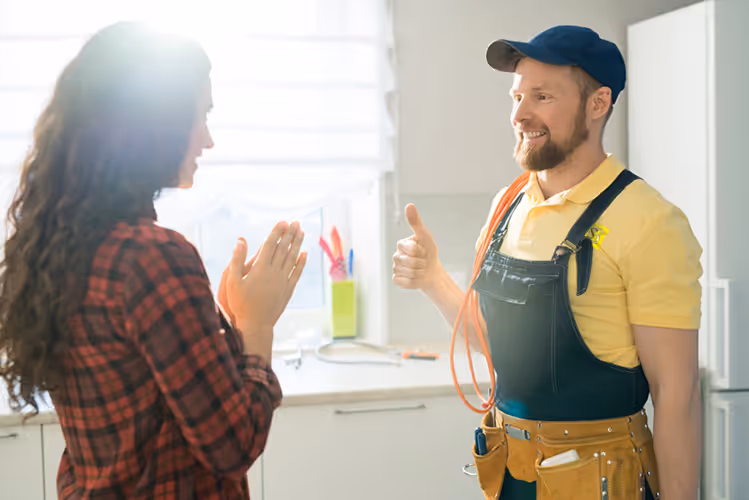 Tenant smiles at technician giving thumbs up after maintenance work in a bright kitchen setting. Happy tenant thanks technician after a successful home repair visit representing quick, reliable maintenance service.