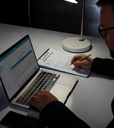 A person works at a desk with a laptop and documents, signing a form, symbolizing the administrative process to successfully find tenant Dubai.