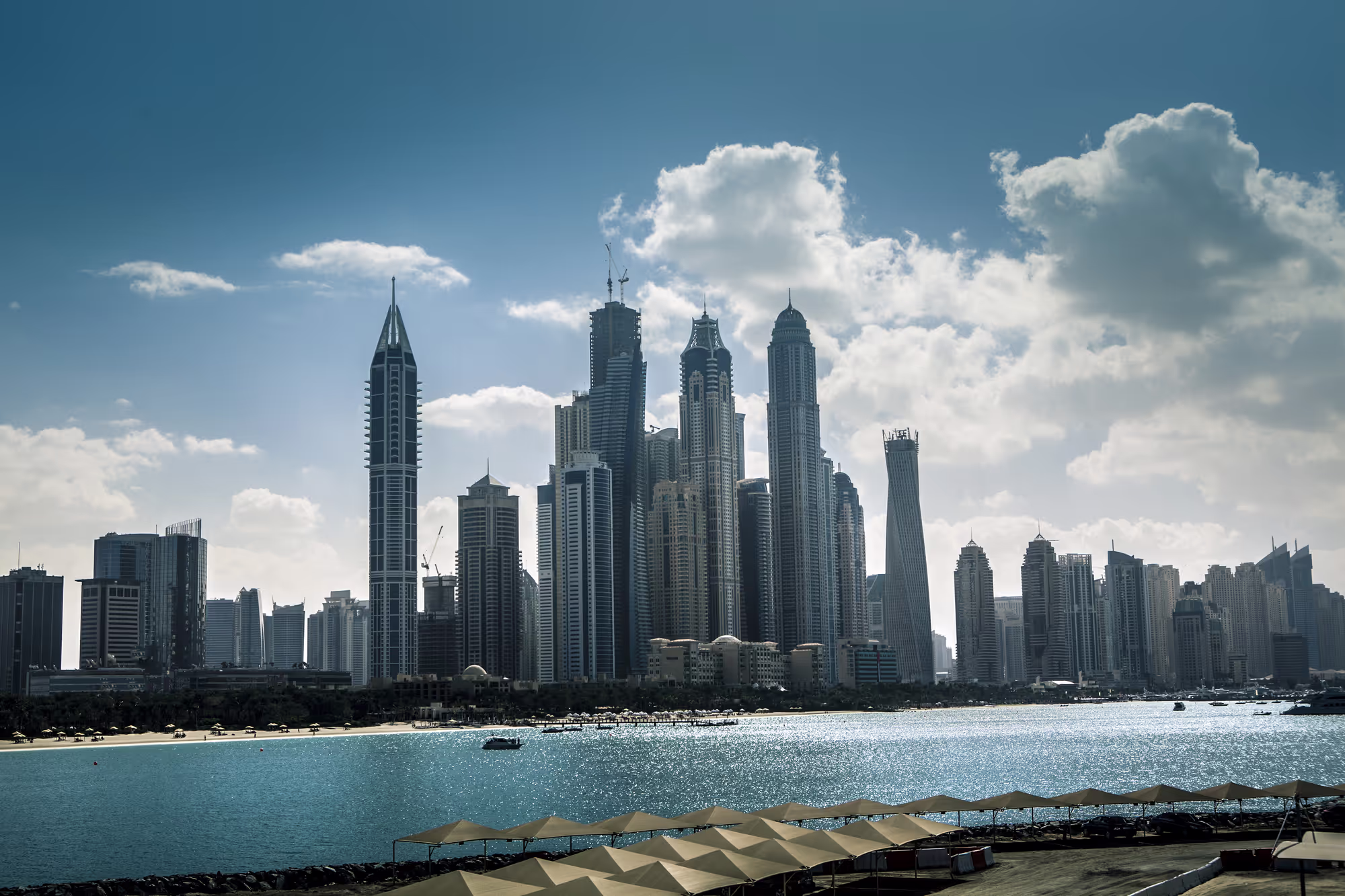 A wide-angle view of the impressive, sunlit skyscraper skyline of the Dubai Marina, showcasing the luxurious options available when buying a property Dubai.