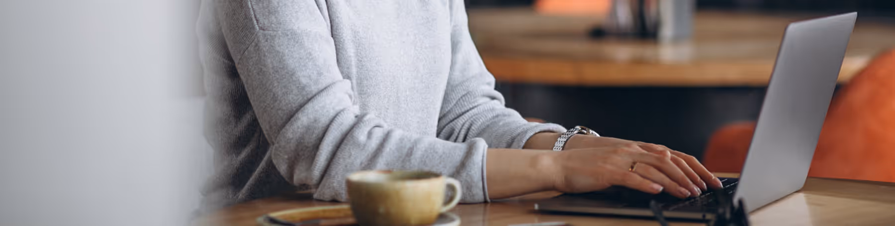 Close-up of woman working on laptop at a cafe table with coffee, efficiently managing digital paperwork like an ejari online registration.