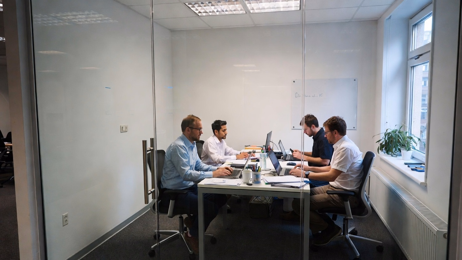 SMALL CONFERENCE ROOM, three people seated around a small table inside a gl
