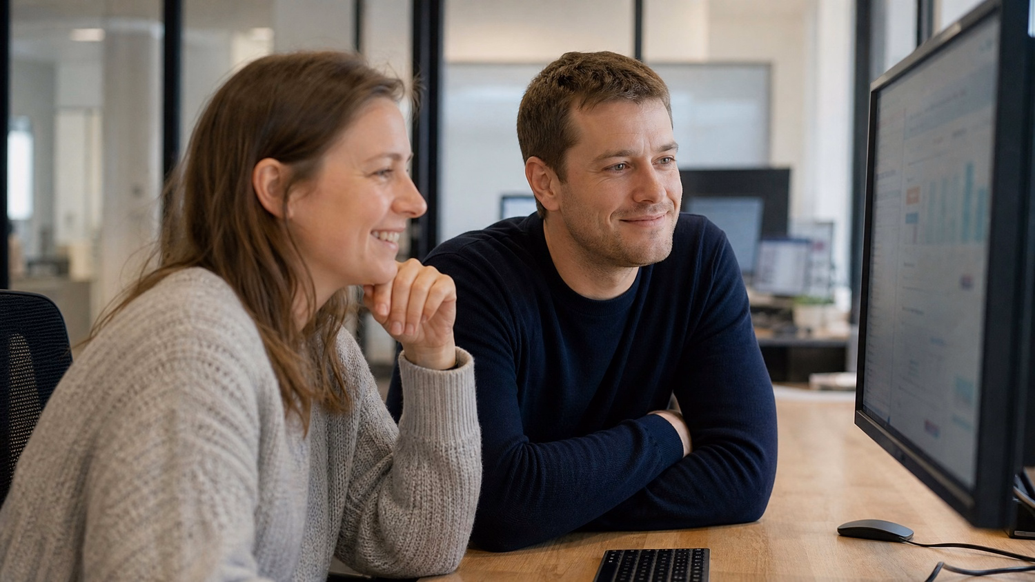 Two people review monitor at table, coffee mug present