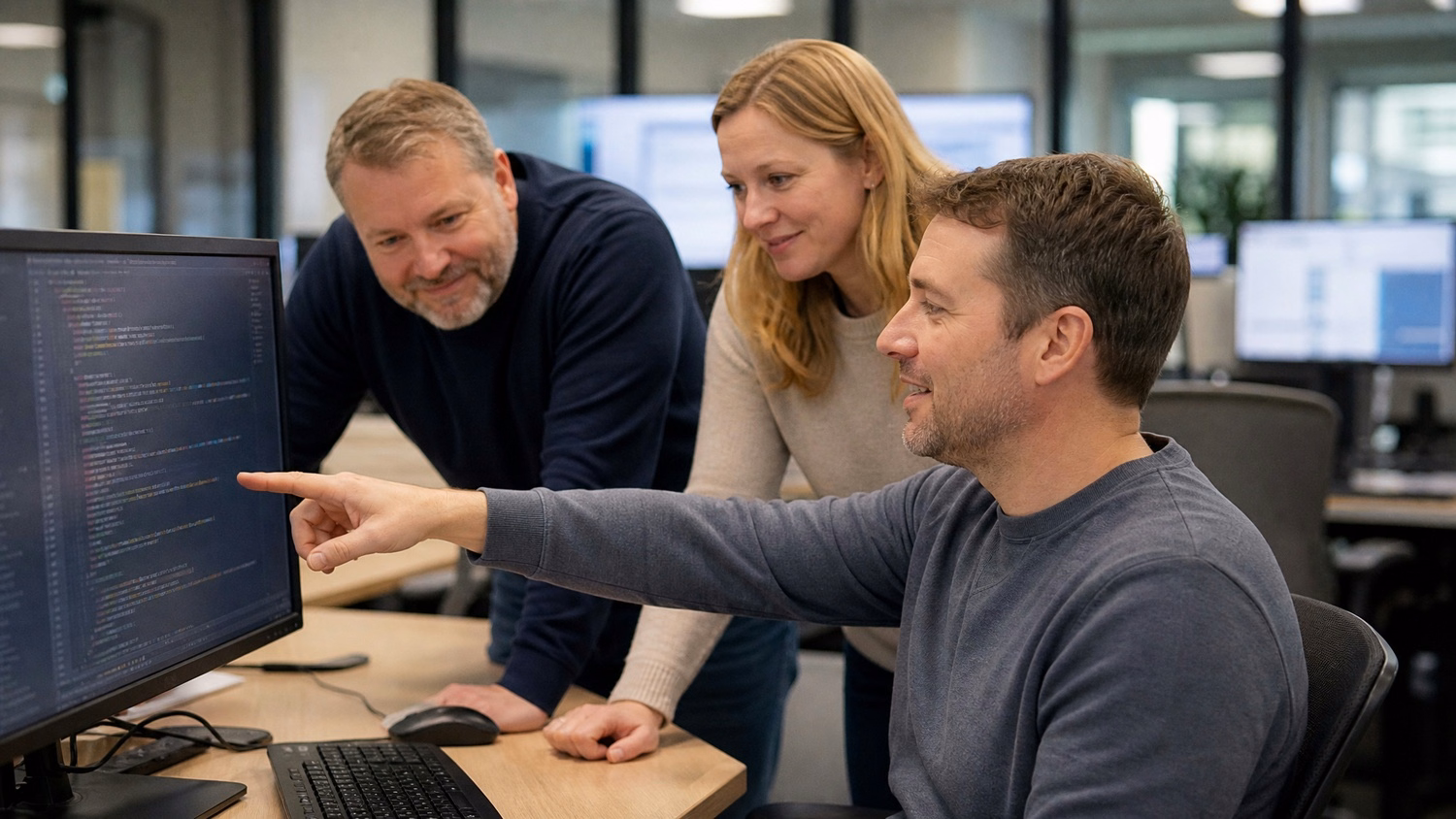 Team reviewing code on monitor, IT professionals collaborating