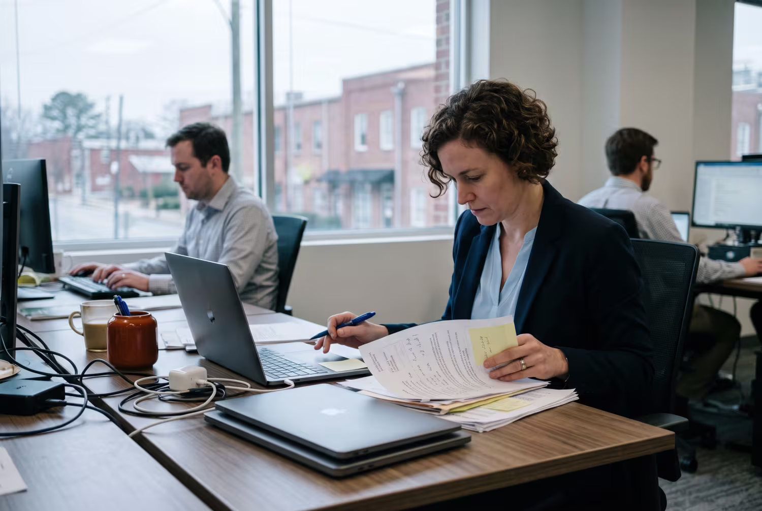 Professional examining paperwork at desk with closed MacBooks in office