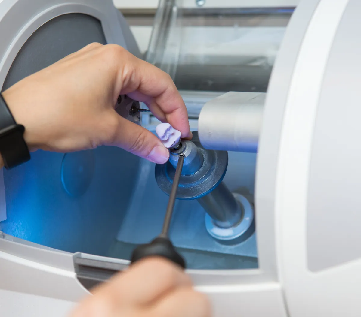 Hand holding a dental mold inside a dental milling machine used for precise tooth restorations.