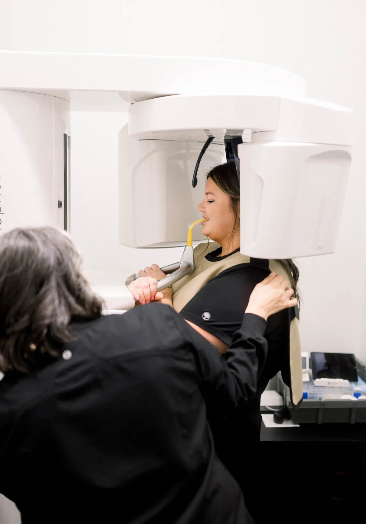 Dental patient positioned in a panoramic X-ray machine with a technician assisting her.