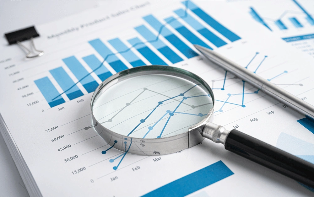 Lupe und Stift liegen auf einem Finanzdiagramm zur Analyse von Fördermitteln