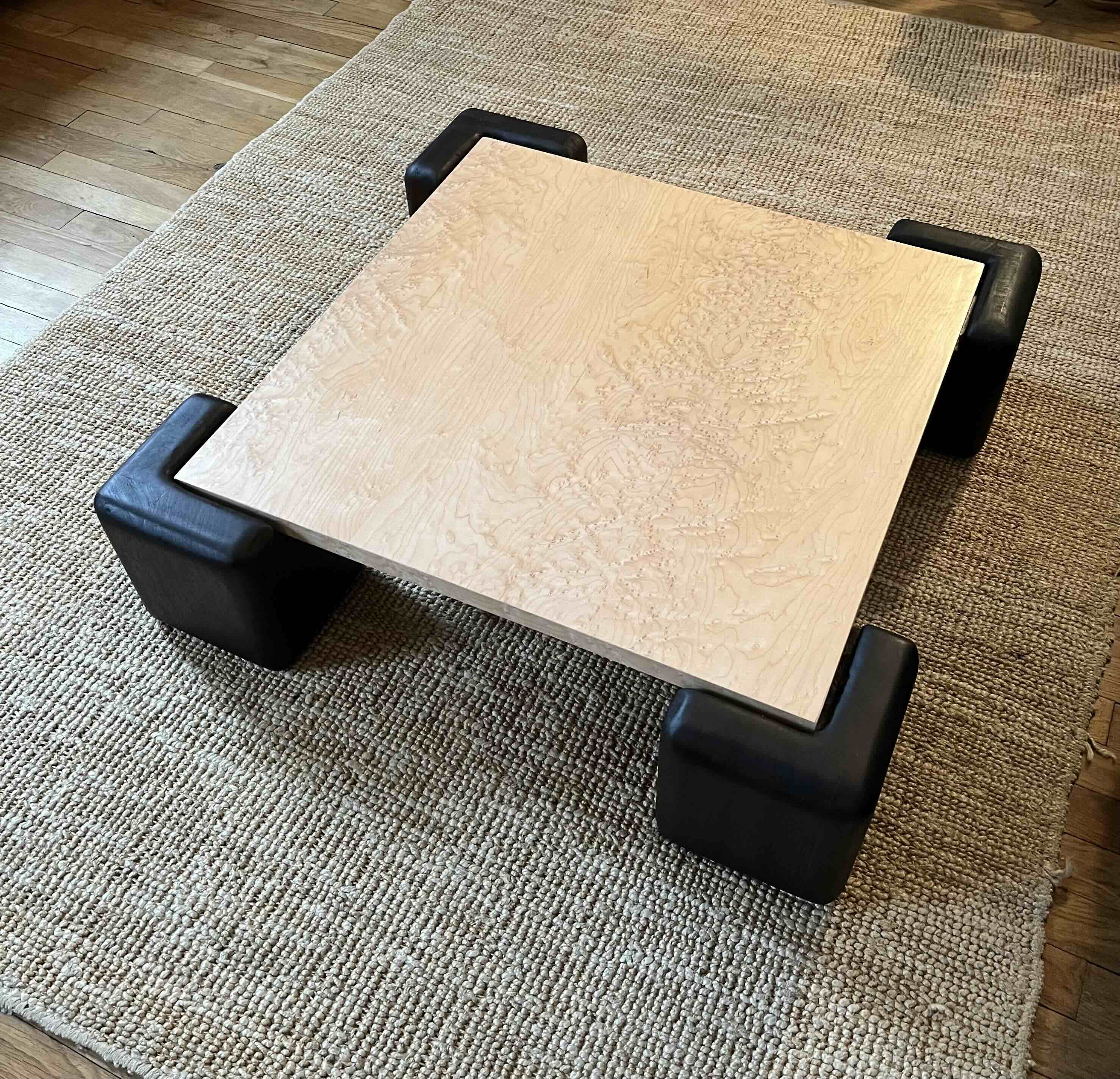 Table basse avec plateau plaqué en érable moucheté vernis, pieds en iroko massif teinté et huilé.