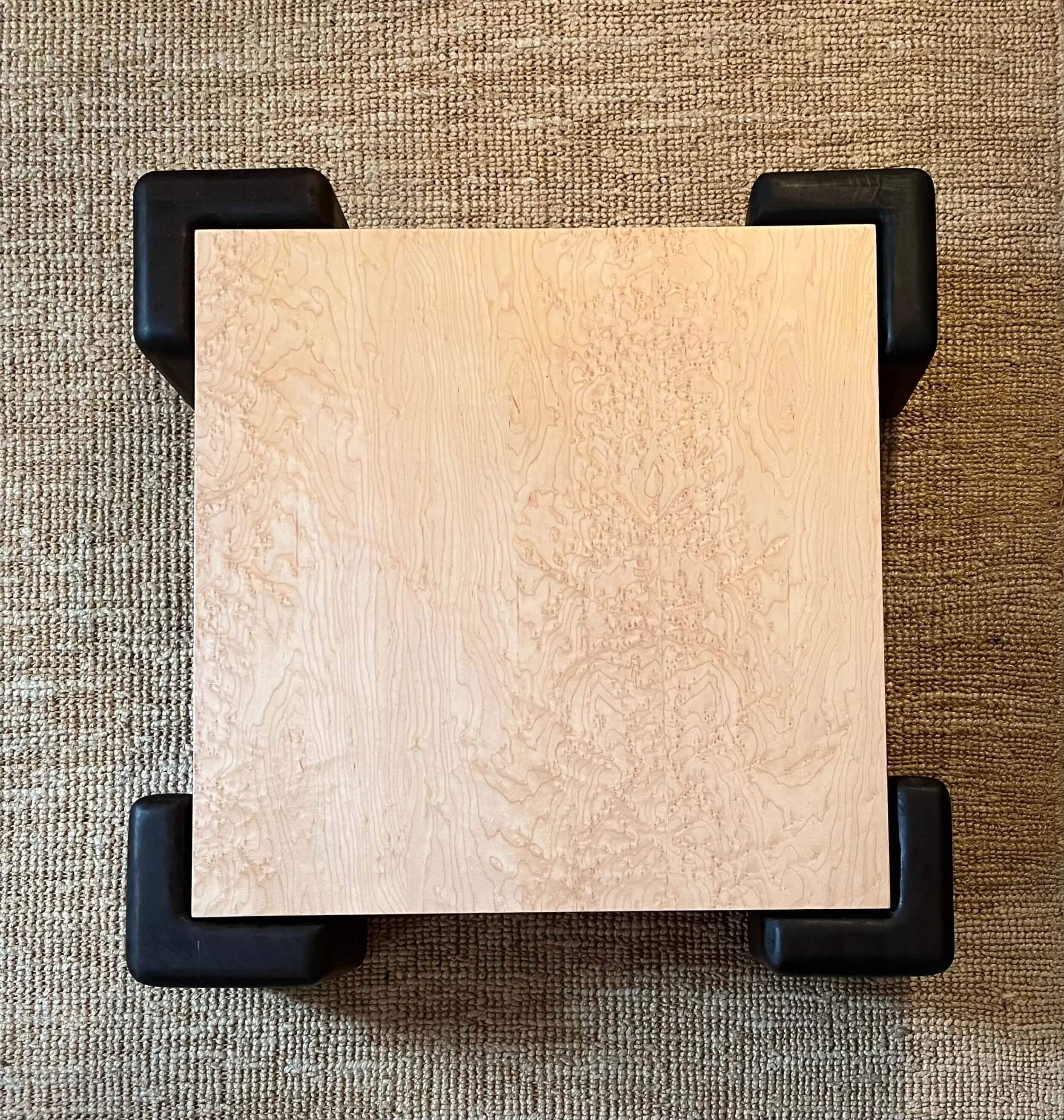 Table basse avec plateau plaqué en érable moucheté vernis, pieds en iroko massif teinté et huilé.