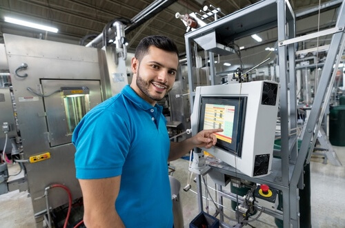 Ein Mann in blauem Poloshirt bedient in einer Fabrik eine Maschine mit Touchscreen.